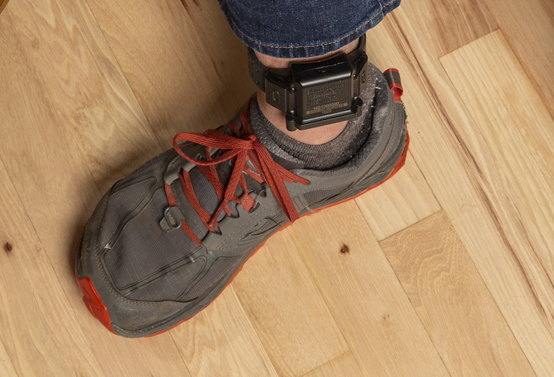 A man with a BI HomeGuard 20|20 ankle monitor, showcasing absence/presence radio frequency monitoring technology.
