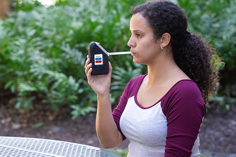 Woman using BI SoberTech alcohol monitoring device blows into straw to submit breath alcohol test.