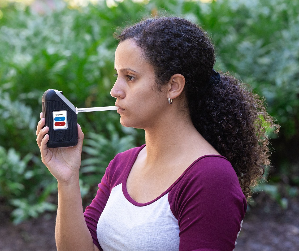 Woman using BI SoberTech alcohol monitoring device blows into straw to submit breath alcohol test.